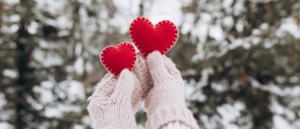 Winter Date-Ideen: Hände in Handschuhen halten zwei rote dekorative Herzen in Winterlandschaft