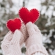 Winter Date-Ideen: Hände in Handschuhen halten zwei rote dekorative Herzen in Winterlandschaft