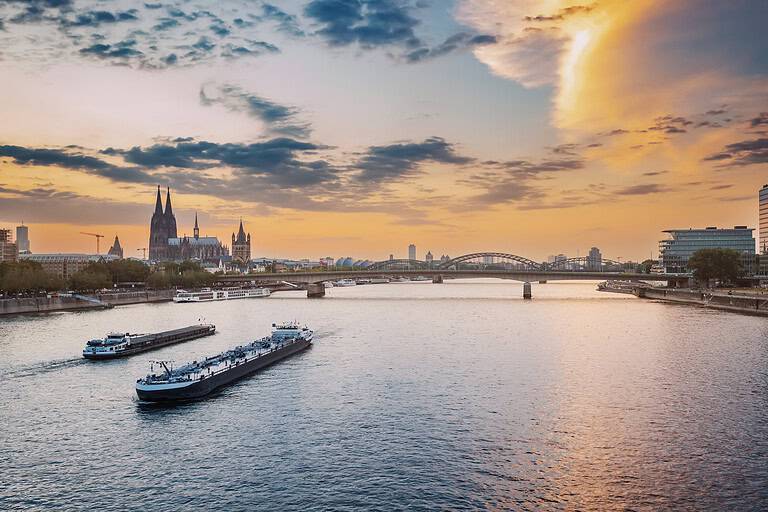 Date-Ideen in NRW: Stadtansicht der Stadt Köln, des Rheins, der Brücken und verschiedener Kähne und Schiffe während des Sonnenuntergangs.